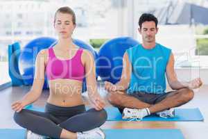 Couple sitting in lotus posture and eyes closed at fitness studi