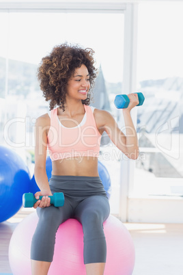 Woman exercising with dumbbells on fitness ball in gym