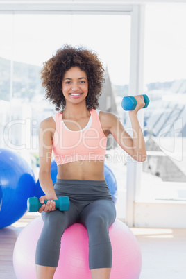 Woman exercising with dumbbells on fitness ball gym