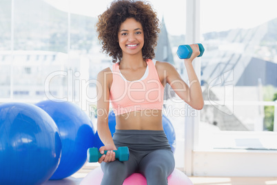 Woman exercising with dumbbells on fitness ball in gym