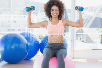 Woman exercising with dumbbells on fitness ball in gym