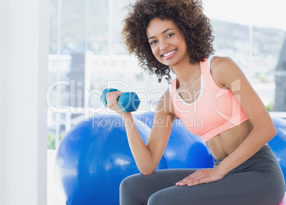 Smiling young woman exercising with dumbbell in gym