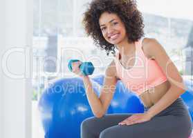 Smiling young woman exercising with dumbbell in gym