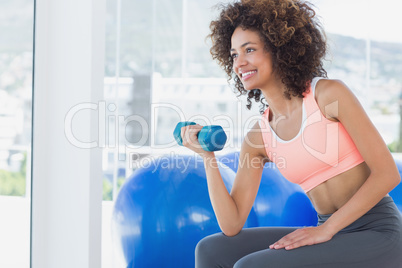 Smiling young woman exercising with dumbbell in gym