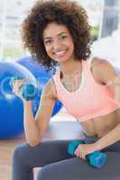 Smiling young woman exercising with dumbbells in gym