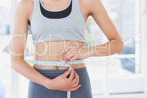 Mid section of a woman measuring waist in fitness studio