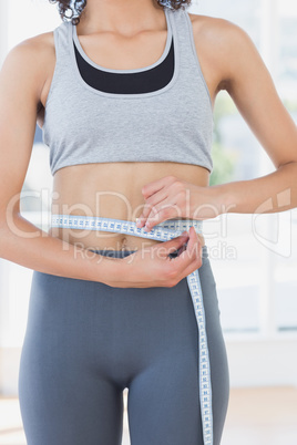 Mid section of a sporty woman measuring waist in fitness studio
