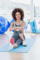 Fit woman sitting on exercise mat in fitness studio