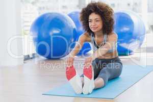 Sporty woman stretching hands to legs in fitness studio
