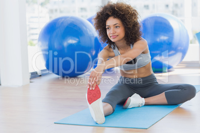Sporty woman stretching hands to leg in fitness studio