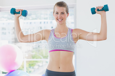 Smiling woman exercising with dumbbells in fitness studio