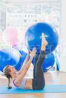 Sporty woman holding exercise ball between legs in fitness studi