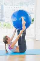 Sporty woman holding exercise ball between ankles in fitness stu