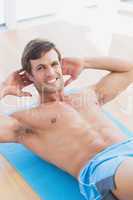 Smiling shirtless man doing sit ups in fitness studio