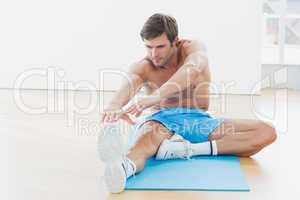 Sporty man stretching hands to leg in fitness studio
