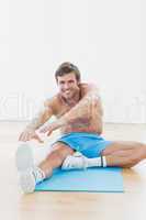 Sporty man stretching hands to leg in fitness studio