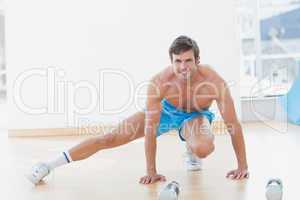 Sporty shirtless young man exercising in fitness studio