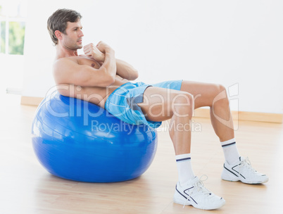 Shirtless man exercising on fitness ball in gym