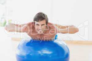 Smiling shirtless man exercising on fitness ball in gym