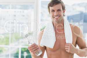 Smiling shirtless man holding water bottle in fitness studio
