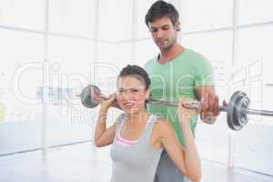 Instructor helping woman to lift barbell in gym