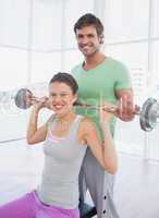 Instructor helping fit woman to lift barbell in gym