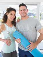 Happy couple holding water bottle and exercise mat