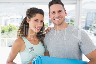 Couple holding water bottle and exercise mat at gym