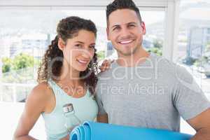 Couple holding water bottle and exercise mat at gym