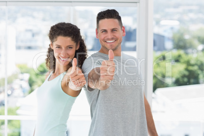 Couple gesturing thumbs up in exercise room