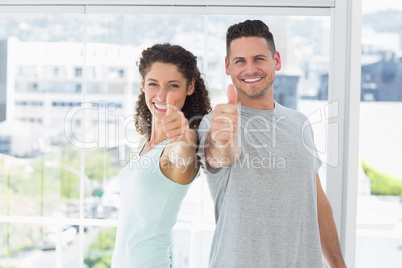 Couple gesturing thumbs up in bright exercise room