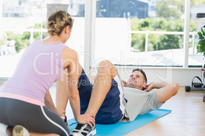Trainer assisting fit man in doing sits