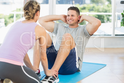 Trainer helping fit man in doing sits up