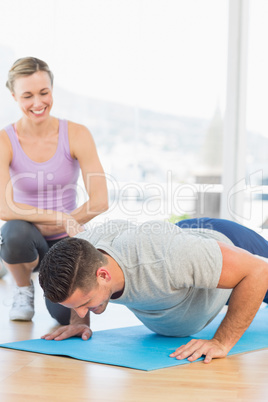 Smiling trainer assisting man with push ups