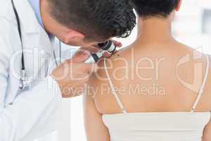 Dermatologist examining mole on back of woman
