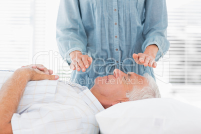 Therapist performing Reiki over senior man