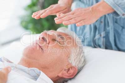 Therapist performing Reiki over senior man