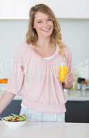 Woman with salad holding orange juice in kitchen
