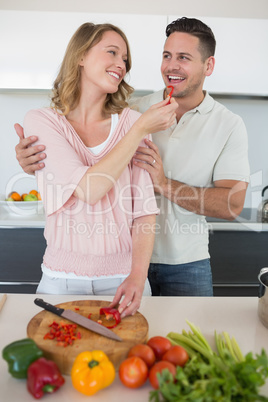 Woman feeding capsicum to man in kitchen