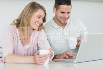 Couple with coffee mugs using laptop at table
