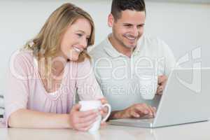 Couple with coffee mugs using laptop at table