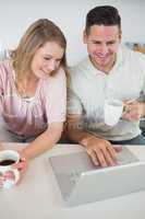 Couple using laptop while holding coffee cups