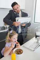 Businessman multi tasking while daughter having breakfast