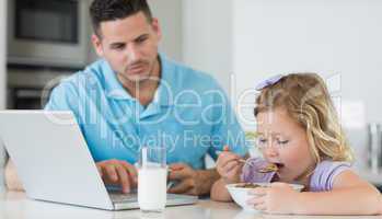 Father looking at daughter having breakfast