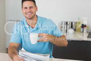 Man with newspaper holding coffee cup at table