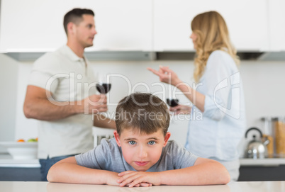 Sad boy leaning on table while parents arguing