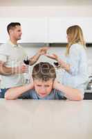 Irritated boy covering ears while parents arguing
