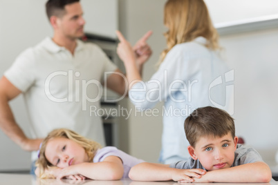 Children leaning on table while parents arguing