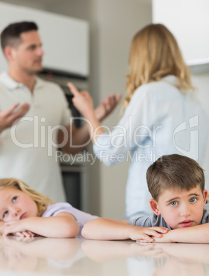 Sad children leaning on table while parents arguing