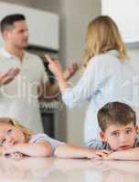 Sad children leaning on table while parents arguing